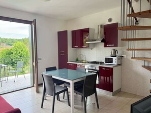 A modern kitchen with a dining area, a balcony with chairs, and a view of greenery. - App.12- Le Terrazze del Garda Immobili e Soluzioni (Manerba del Garda)