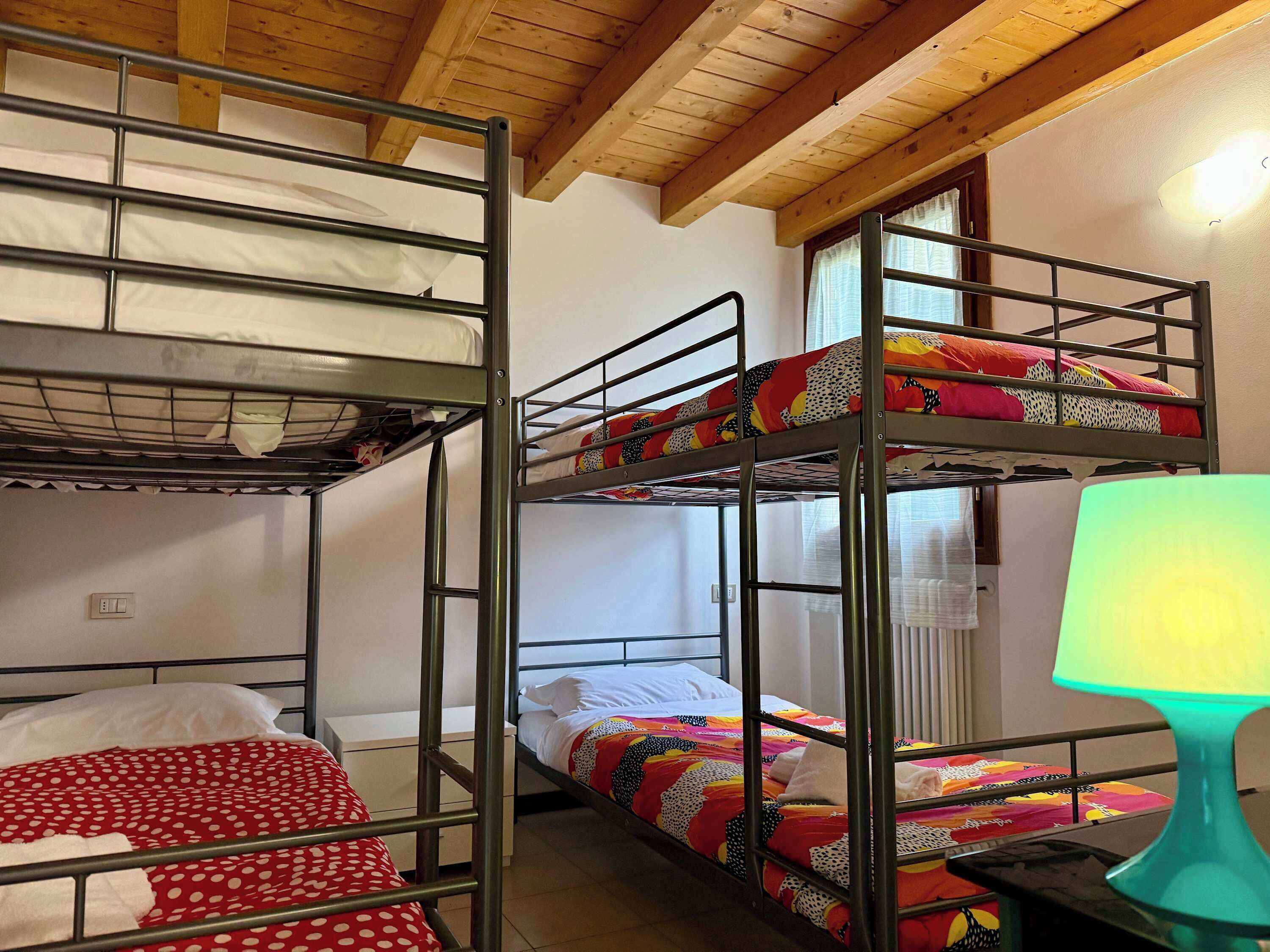 A bunk bed room with a wooden ceiling, a window with curtains, and a bedside lamp.