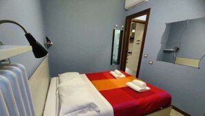 Ett hotellrum med en säng, en spegel, ett element och en hylla som är monterad på väggen.