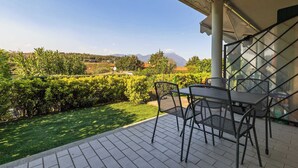 Une terrasse avec une table et des chaises, une vue sur un jardin et un bâtiment doté d’une zone abritée.