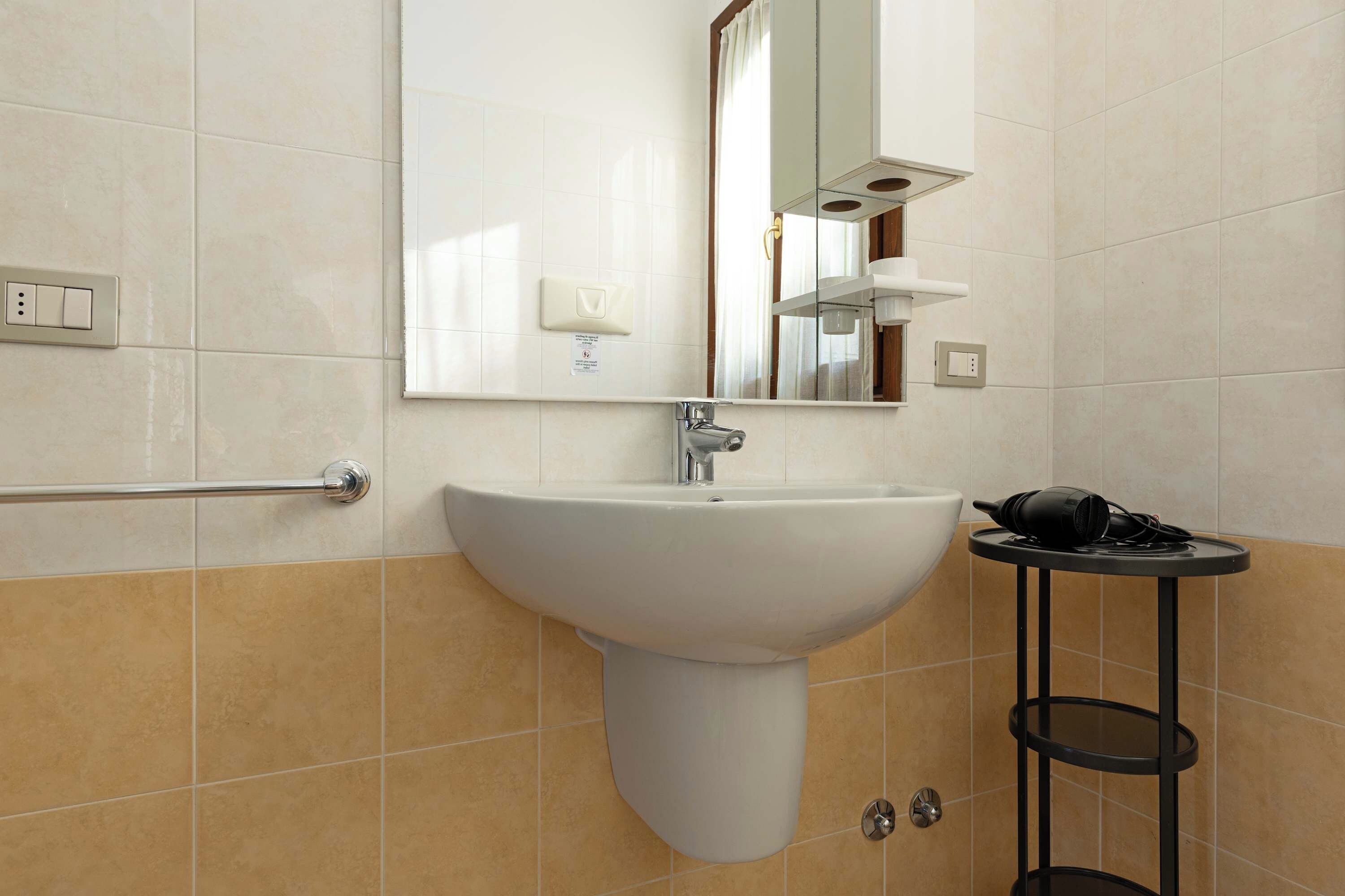 Un bagno con un lavandino bianco, uno specchio, un portascopevoli e un piccolo tavolo con un asciugacapelli.
