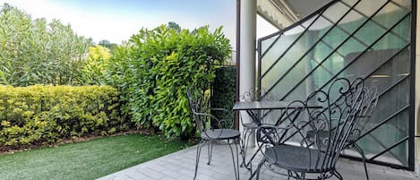 A patio with a table and chairs, surrounded by a well-maintained hedge and a grassy area.