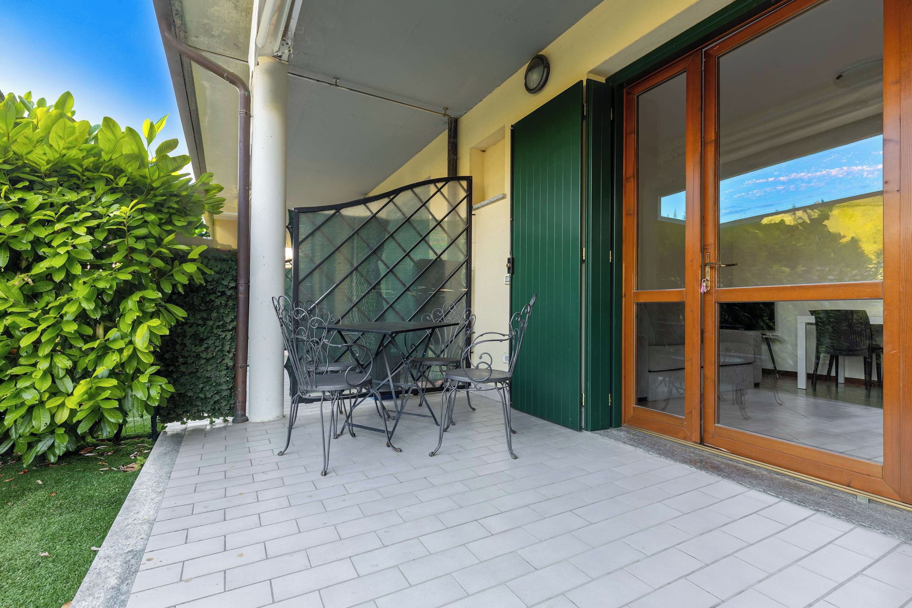A patio area with a metal table and chairs, a green door, and a view of the interior.