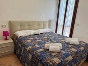 A bedroom with a bed, pillows, a nightstand with a lamp, and a window with curtains. - App.3- Le Terrazze del Garda Immobili e Soluzioni (Manerba del Garda)