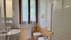 Un baño con lavabo, inodoro, bidé y ventana con cortinas.