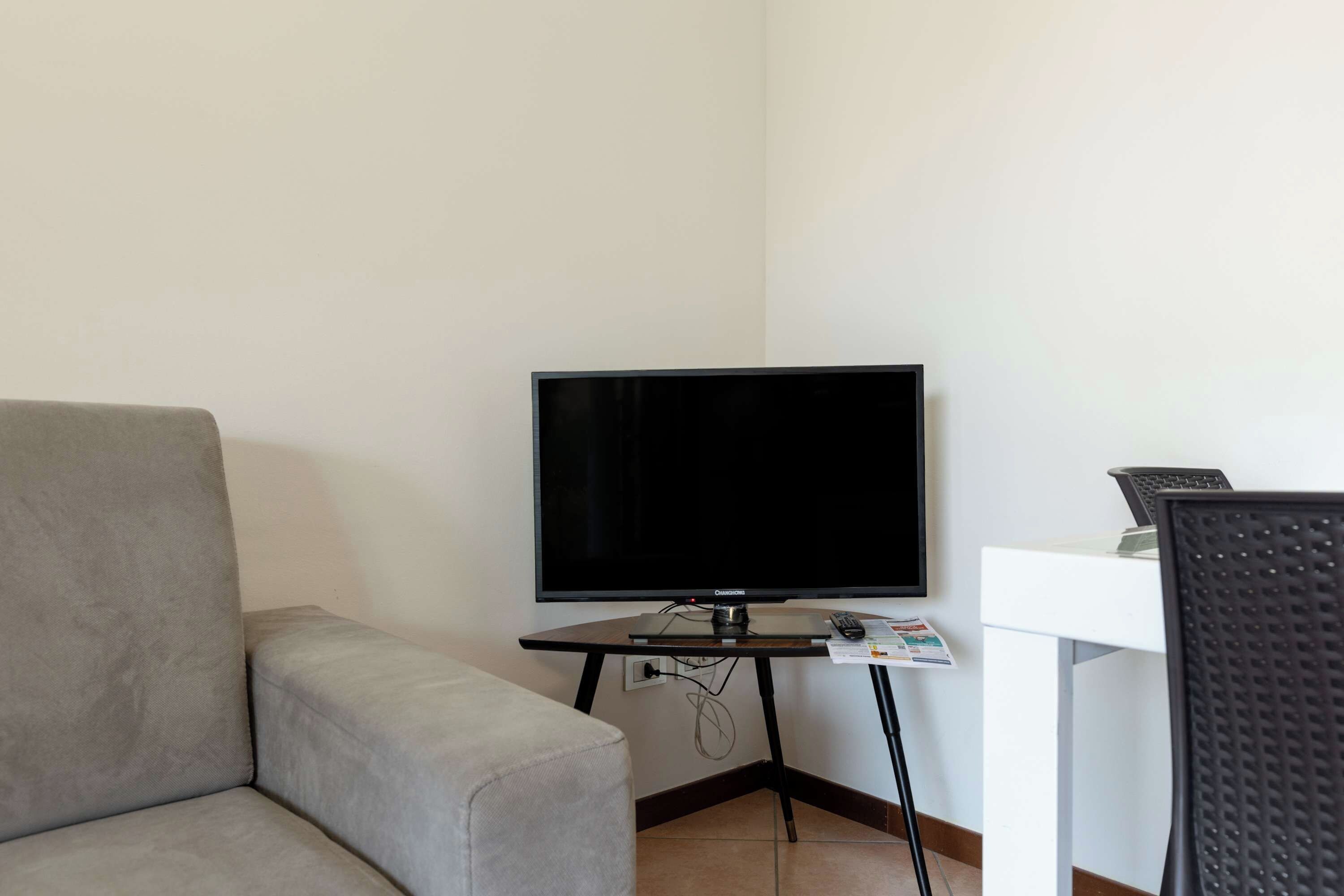 Una habitación con un sofá gris, un televisor sobre un mueble bajo y un escritorio blanco con un teclado y un ratón.