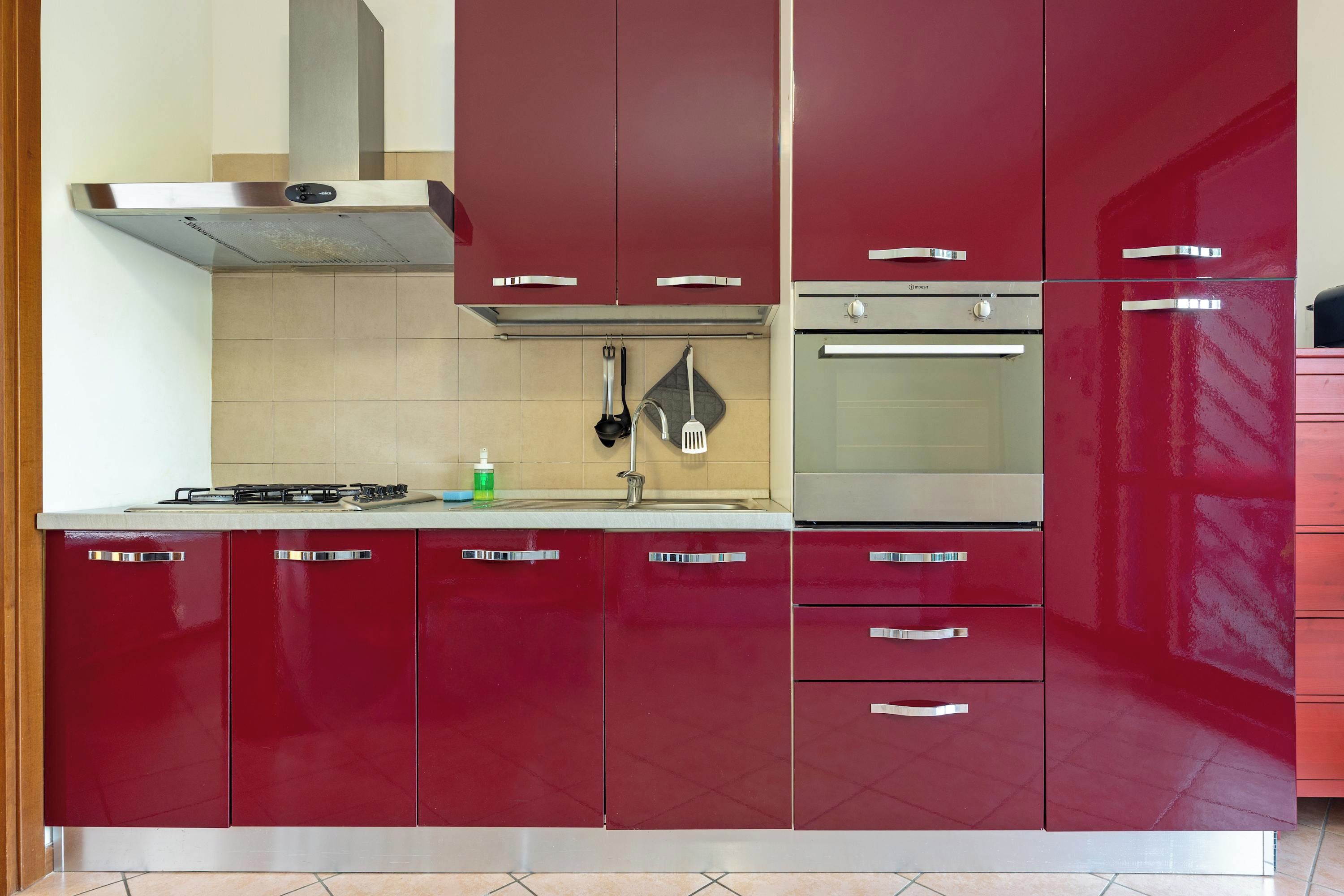 A kitchen with red cabinets, a gas stove, a stainless steel range hood, and a built-in oven.