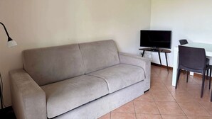 Una sala de estar con un sofá, un televisor y una mesa de comedor con sillas.