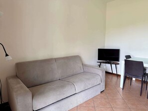 Ein Wohnzimmer mit einer Couch, einem Fernseher und einem Esstisch mit Stühlen.