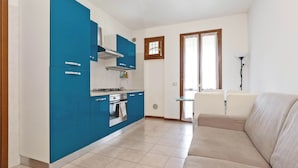 Una cocina moderna con armarios azules, un horno empotrado y una zona de comedor con un sofá color beige.