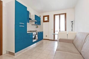 Eine moderne Küche mit blauen Schränken, einem eingebauten Backofen und einem Essbereich mit einem beigefarbenen Sofa.
