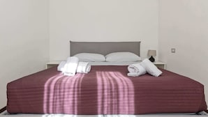 Una cama bien hecha con una colcha roja, almohadas blancas y toallas dobladas a un lado.