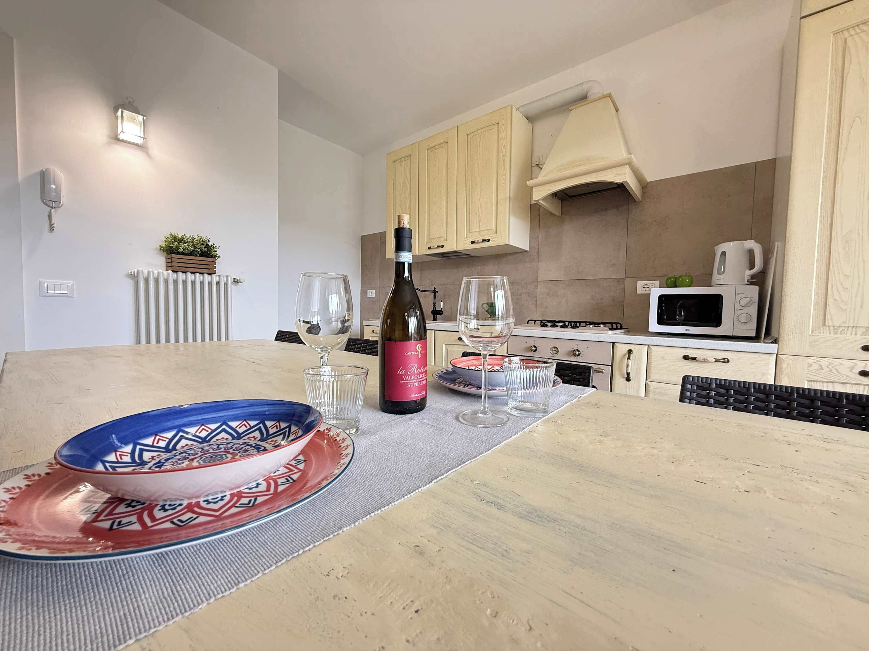 A kitchen with a dining table, a wine bottle, glasses, and a microwave.