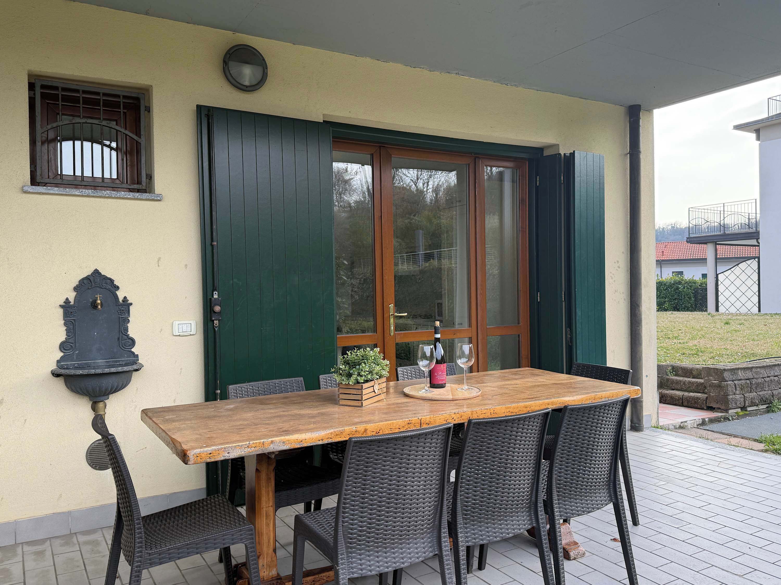 A patio with a wooden table and wicker chairs, a green door, and a small window with bars.