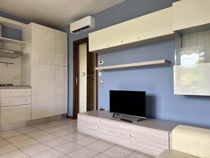 A modern living room with a flat-screen TV, built-in cabinets, and a kitchen area. - App.1- Le Terrazze del Garda Immobili e Soluzioni (Manerba del Garda)