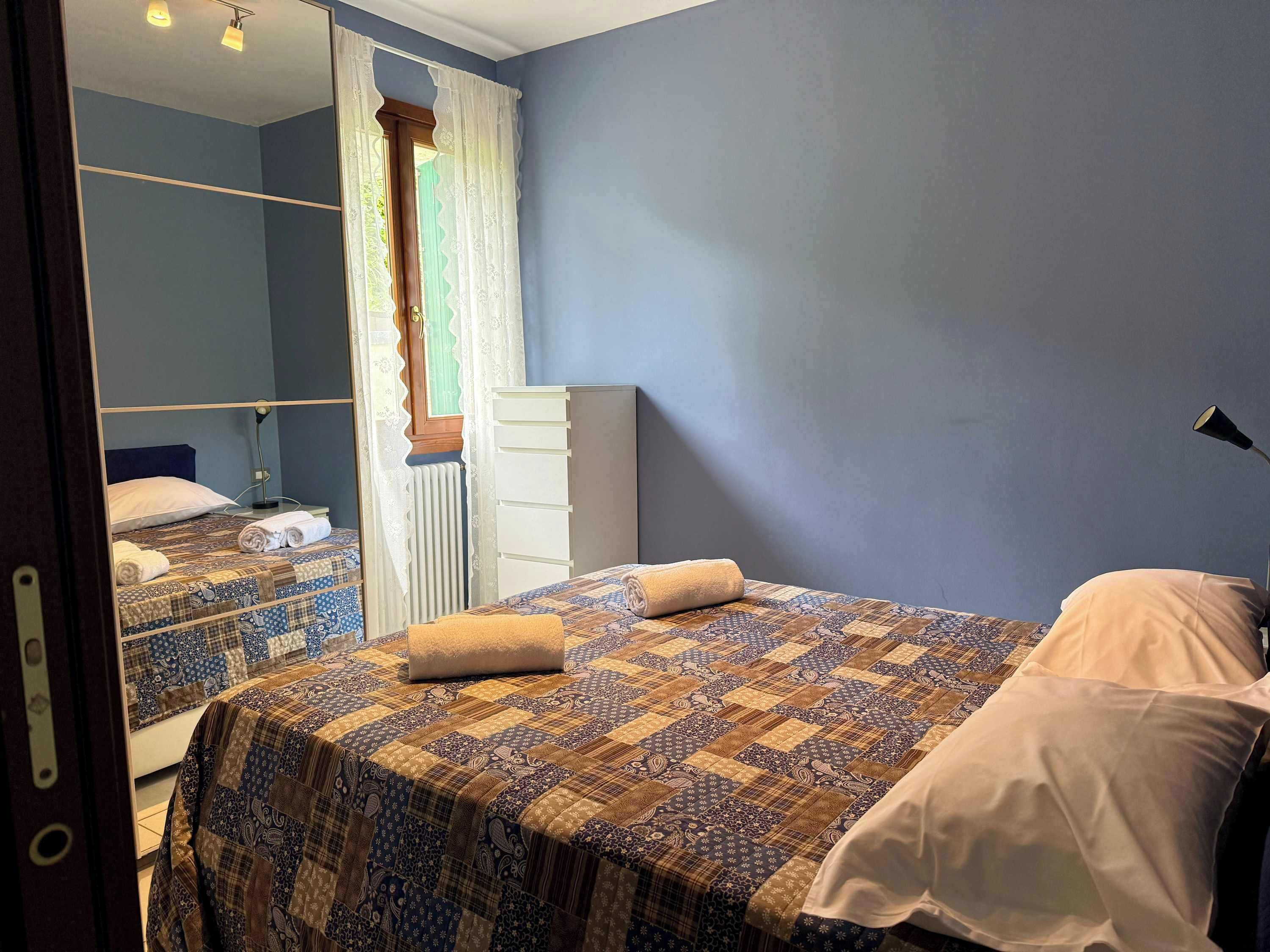 Une chambre à coucher avec un lit, une commode, un miroir et une fenêtre avec des rideaux.