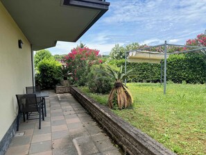 Eine Terrasse mit Tisch und Stühlen, einem Blumentopf und einem Garten mit rosa Blumen und einem Palmenbaum.