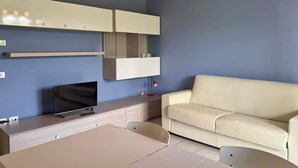 Una sala de estar moderna con televisor de pantalla plana, un sofá color beige, una mesa de comedor y armarios empotrados.