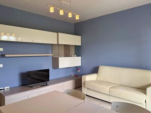 Ein modernes Wohnzimmer mit Fernseher, einem beigefarbenen Sofa, einem Esstisch und Einbauschränken.