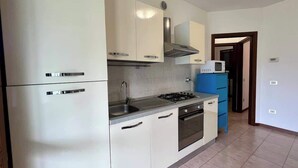 Una cocina con armarios blancos, una estufa a gas, un microondas y un mueble azul.