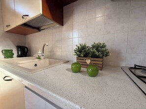 A kitchen with a white countertop, a sink, a coffee maker, and a wooden planter with green peppers. - App.10- Le Terrazze del Garda Immobili e Soluzioni (Manerba del Garda)