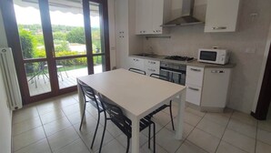 Une cuisine équipée d’une table à manger, de chaises, de placards, d’un four à micro-ondes et offrant une vue à travers la porte vitrée.