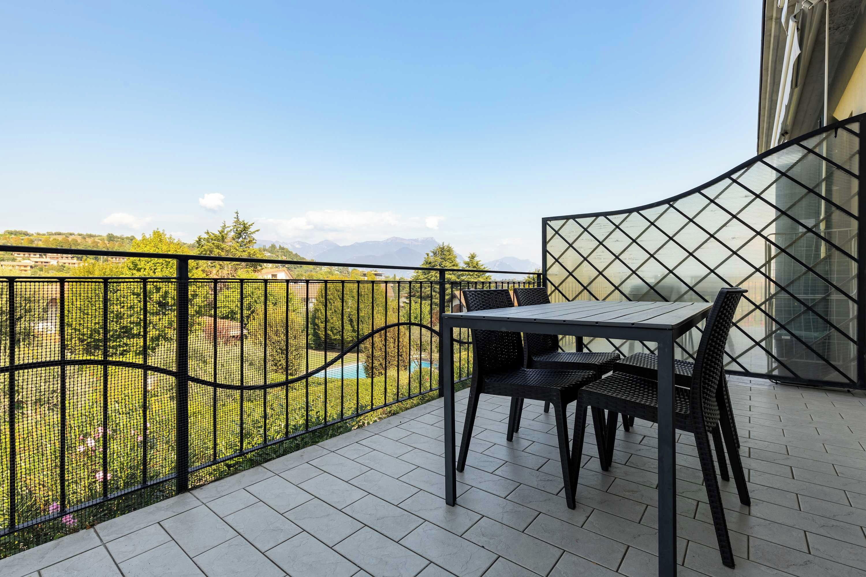 Un balcon avec une table et des chaises, une vue sur un paysage verdoyant et une clôture en métal.