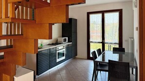 A modern kitchen with a built-in microwave, oven, and gas stove. There is a dining table with chairs and a view of the outside through a large window. - App.11- Le Terrazze del Garda Immobili e Soluzioni (Manerba del Garda)