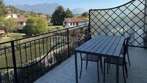 A balcony with a table and chairs, a view of houses and mountains, and a metal fence. - App.11- Le Terrazze del Garda Immobili e Soluzioni (Manerba del Garda)