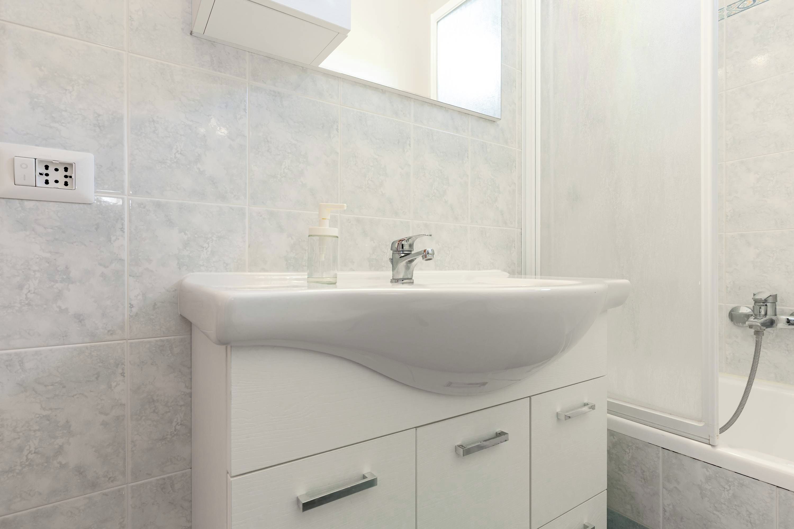 A bathroom with a white sink, a mirror above it, and a shower area.