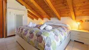 A bedroom with a wooden ceiling, a bed with a patterned bedspread, a bedside lamp, and a radiator. - App.14- Le Terrazze del Garda Immobili e Soluzioni (Manerba del Garda)