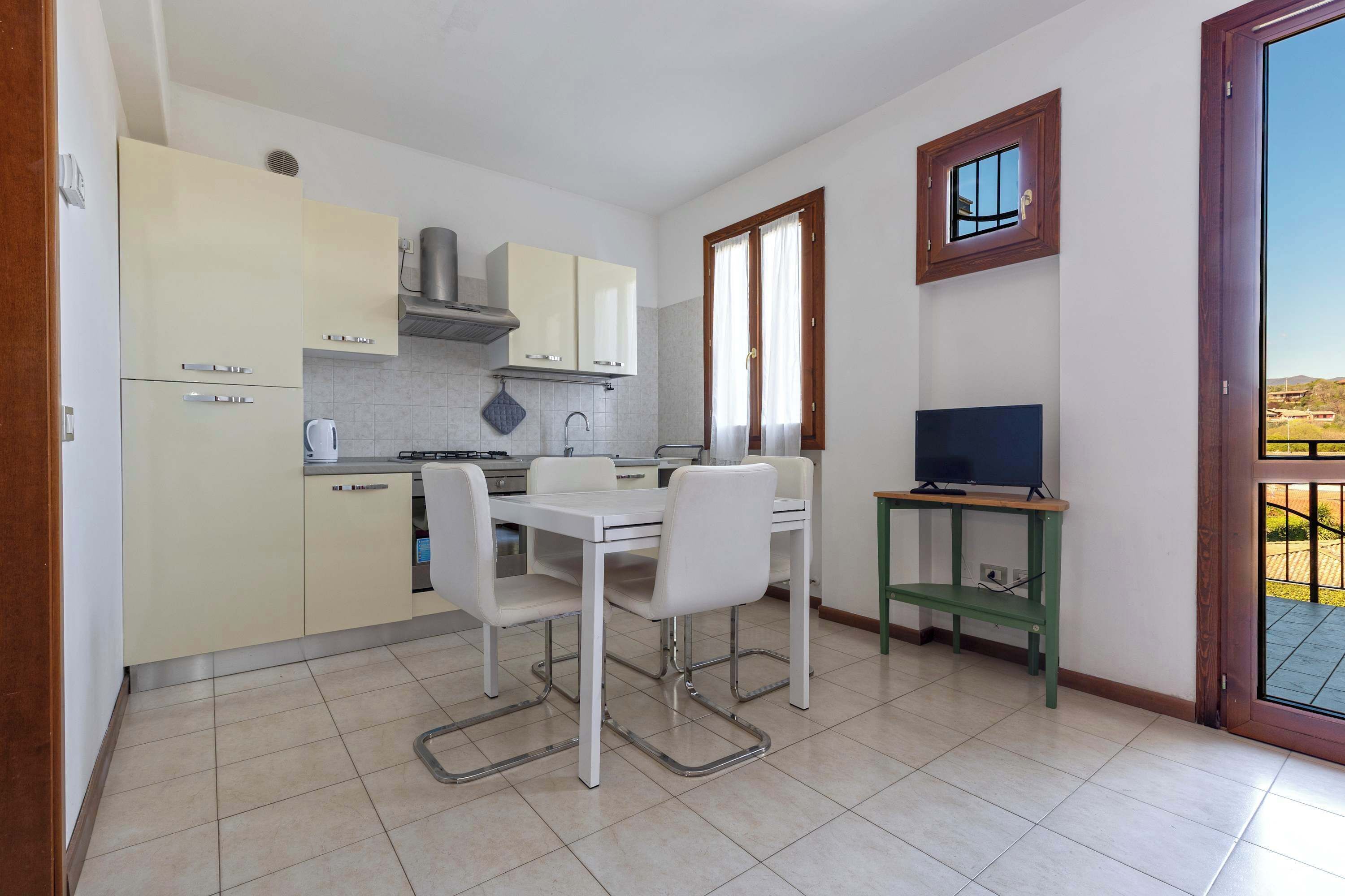 Une cuisine compacte avec une table et des chaises, un petit téléviseur posé sur un meuble, et une fenêtre donnant sur un paysage agréable.