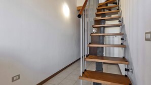 A staircase with wooden steps and metal railings, a light fixture on the wall, and a tiled floor. - App.14- Le Terrazze del Garda Immobili e Soluzioni (Manerba del Garda)