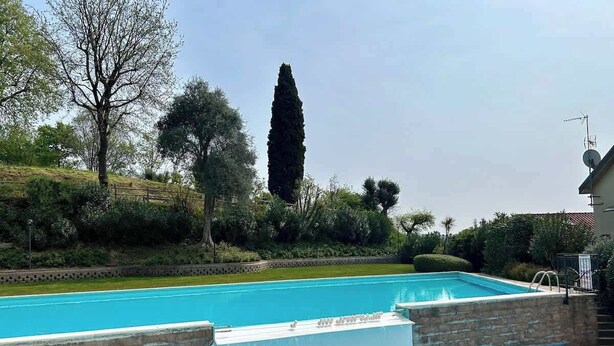 A swimming pool with a stone wall and a metal railing. - App.14- Le Terrazze del Garda Immobili e Soluzioni (Manerba del Garda)