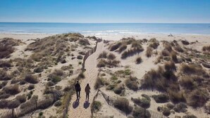 Une plage de sable avec des dunes et une passerelle en bois menant à l’eau.