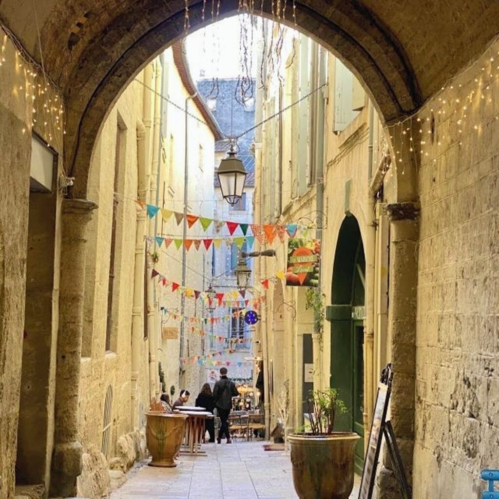 An arched alleyway with stone walls, hanging lights, and colorful flags.