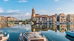 Un port de plaisance avec des bateaux amarrés, une tour imposante et des bâtiments le long du front de mer.