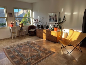 Ein Wohnzimmer mit einem Holzkabinett, einem gelben Sessel, einem Teppich und einem Fenster mit Blick auf Bäume.