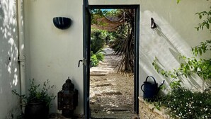 Une porte qui donne sur un jardin avec un chemin de gravier, une lanterne et un arrosoir.