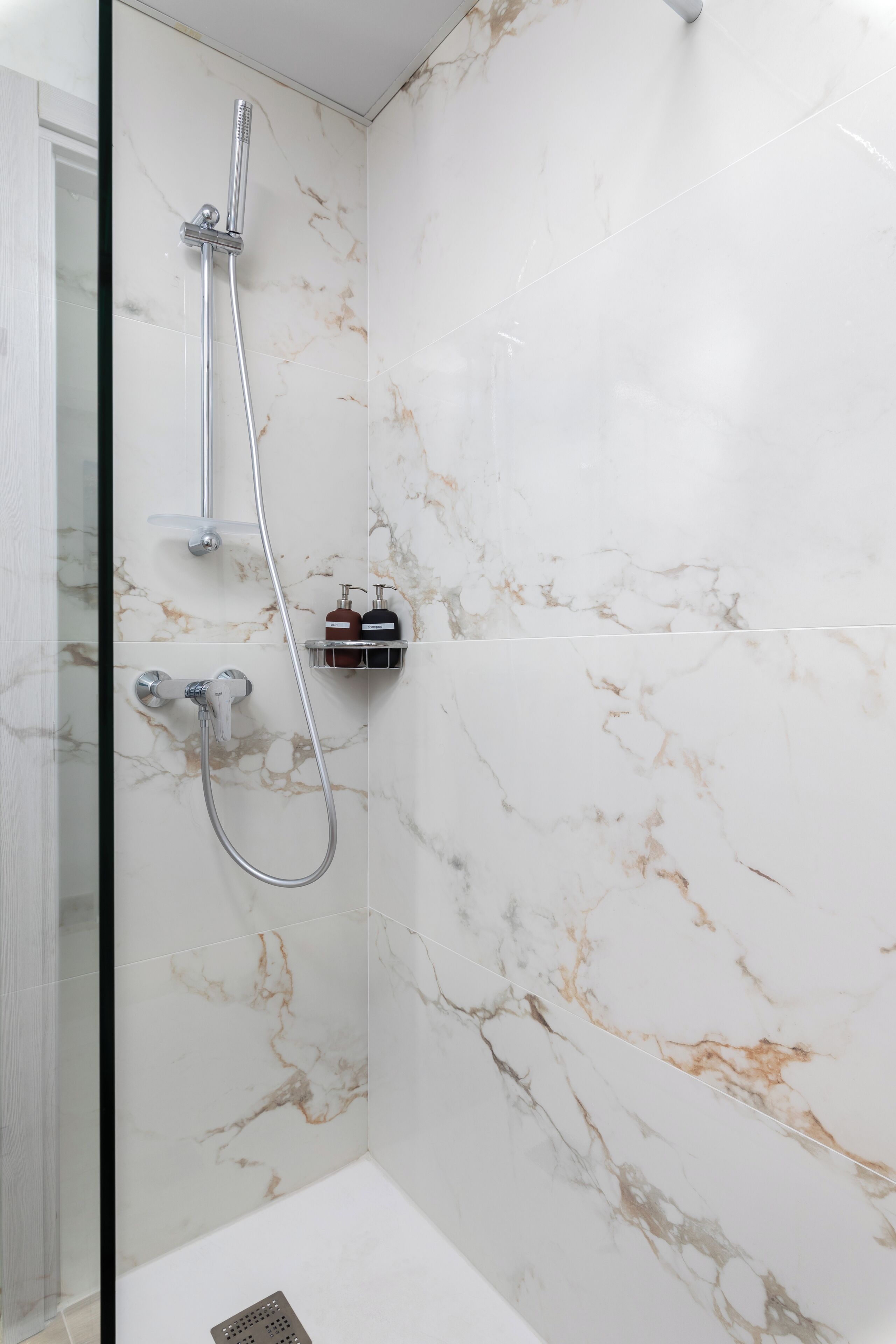 Un baño con ducha, paredes de mármol y un pequeño estante con artículos de tocador.