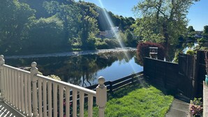 A riverside view with a wooden fence, a grassy area, and a house in the background.