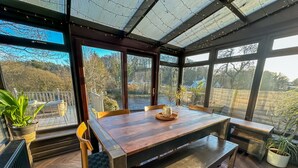 A conservatory with a wooden table, chairs, and potted plants.