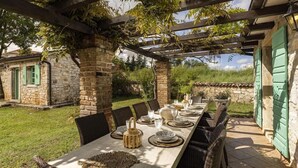 An outdoor dining area with a long table set for six, surrounded by stone walls and greenery. - Le Château B&B (Visnjan)