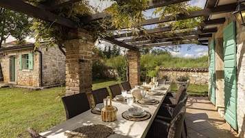 Un espacio de comedor al aire libre con una larga mesa dispuesta para seis personas, rodeado de muros de piedra y follaje.