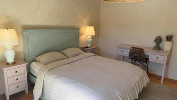 A bedroom with a bed, two bedside tables with lamps, a desk, and a wicker hanging light fixture.