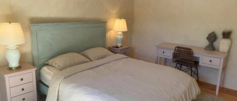 A bedroom with a bed, two bedside tables with lamps, a desk, and a wicker hanging light fixture.