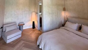 A bedroom with a bed, a chair, a lamp, and a wooden floor. - Le Château B&B (Visnjan)