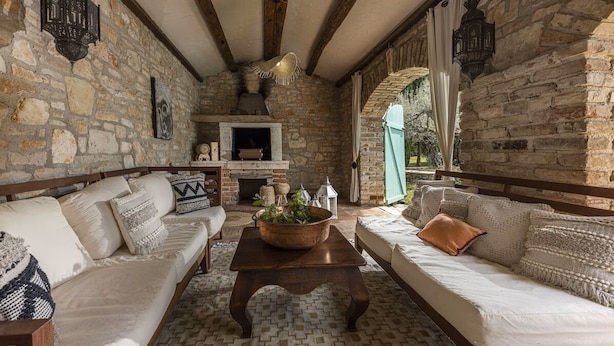 A stone-walled room with a fireplace, a sofa, a coffee table, and a window with a view of greenery. - Le Château B&B (Visnjan)