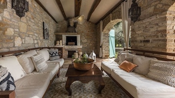 Una habitación con paredes de piedra, una chimenea, un sofá, una mesa de centro y una ventana con vistas al verdor.
