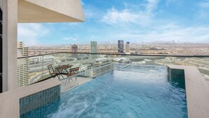 Ein Pool mit unendlicher Aussicht auf das Stadtbild, ausgestattet mit Glastrennwand, Sitzgelegenheit mit Tisch und Stühlen.